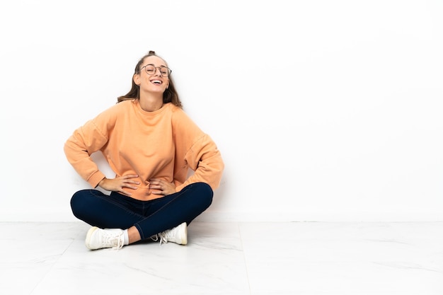 Jeune femme assise sur le sol posant avec les bras à la hanche et souriant