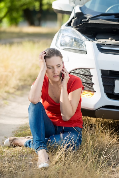 Jeune femme assise sur le sol et s'appuyant sur une voiture cassée