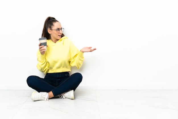 Jeune femme assise sur le sol tenant un café à emporter avec une expression faciale surprise