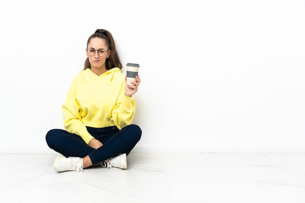 Jeune femme assise sur le sol tenant un café à emporter avec une expression triste