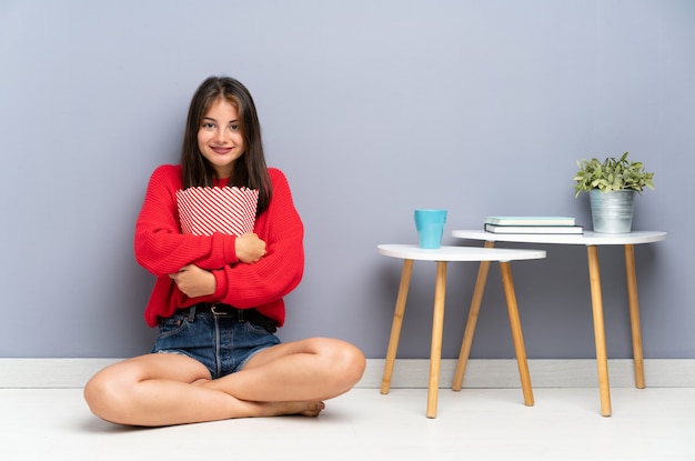 Jeune femme assise sur le sol et tenant des pop-corn