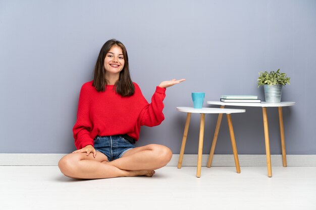 Jeune femme assise sur le sol tenant une surface imaginaire sur la paume