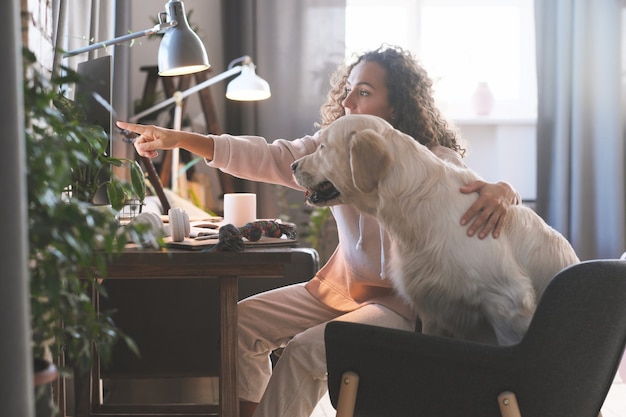 Photo jeune femme assise avec son chien devant l'ordinateur et pointant sur l'ordinateur montrant quelque chose à elle