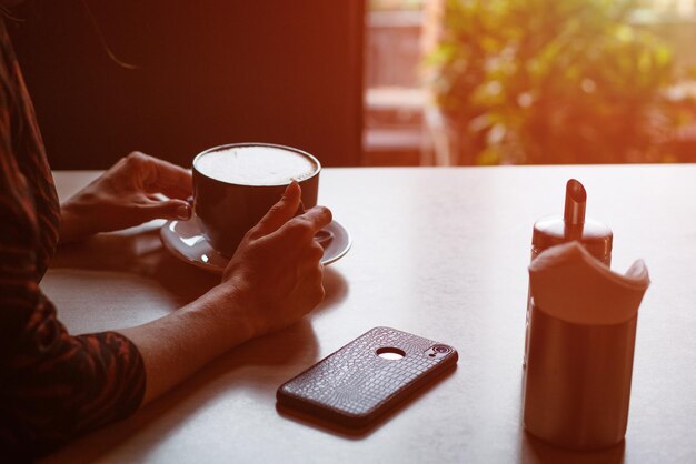 Photo une jeune femme assise à une table avec du café près de la fenêtre.