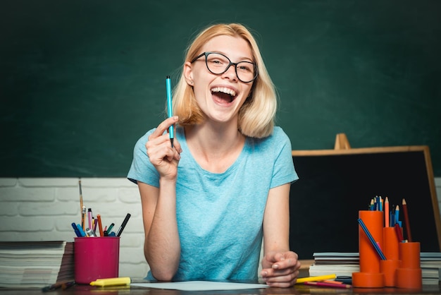 Jeune femme assise à table faisant des devoirs bibliothèque Jeune étudiant heureux Journée mondiale des enseignants Heureuse étudiante décontractée avec sur fond de tableau noir