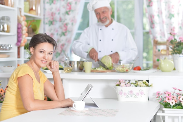 Jeune femme assise à table avec tablette pendant que le chef prépare la salade sur fond