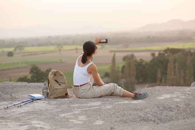 Jeune femme assise avec téléphone portable. Sentier touristique de haute montagne au coucher du soleil.