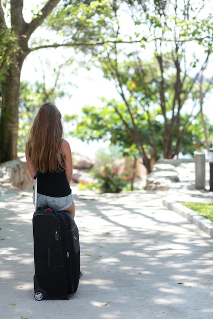 Jeune femme assise sur une valise avec des vêtements et attendant quelqu'un