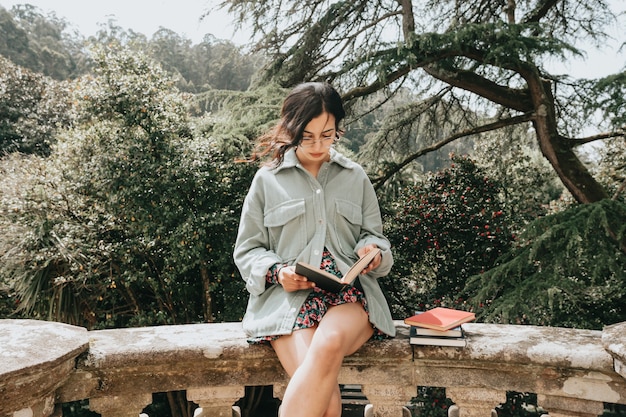 Jeune femme assise sur un vieux bâtiment en lisant un livre pendant une journée ensoleillée