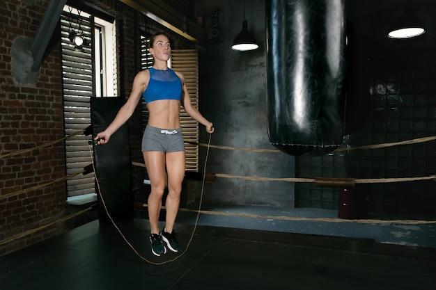 Jeune femme athlétique à la corde à sauter dans une salle de sport de boxe