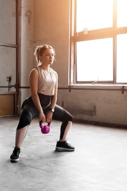 Jeune femme athlétique faisant de l'exercice avec un kettlebell en position accroupie