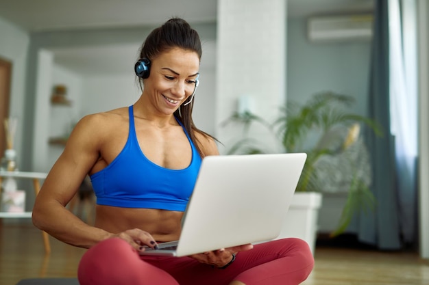 Jeune femme athlétique heureuse utilisant un ordinateur tout en se relaxant sur le sol dans le salon