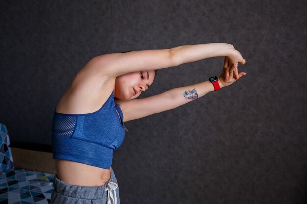 Jeune femme athlétique pratiquant le yoga, l'étirement du corps, l'exercice, l'entraînement, portant des vêtements de sport, un T-shirt bleu, un short, près du canapé à la maison