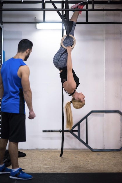 jeune femme athlétique travaillant avec un entraîneur personnel sur des anneaux de gymnastique à la salle de fitness cross