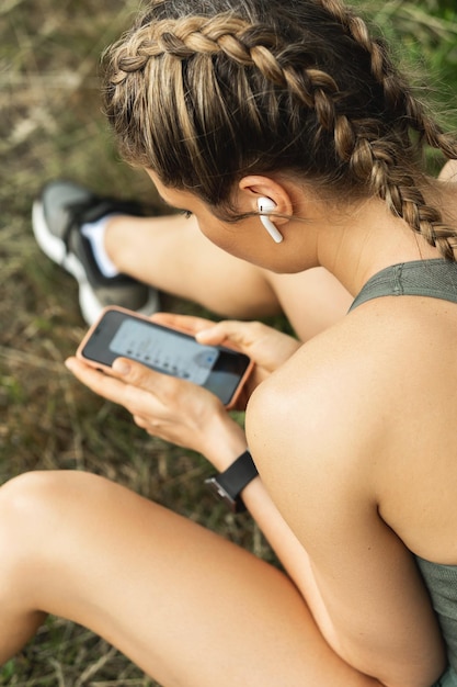 Jeune femme athlétique utilisant un smartphone pendant son entraînement de remise en forme à l'extérieur