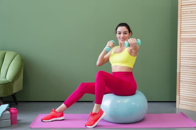 Jeune femme athlétique en vêtements de sport faisant des exercices d'étirement de fitness à la maison dans le salon Concept de sport et de soins du corps