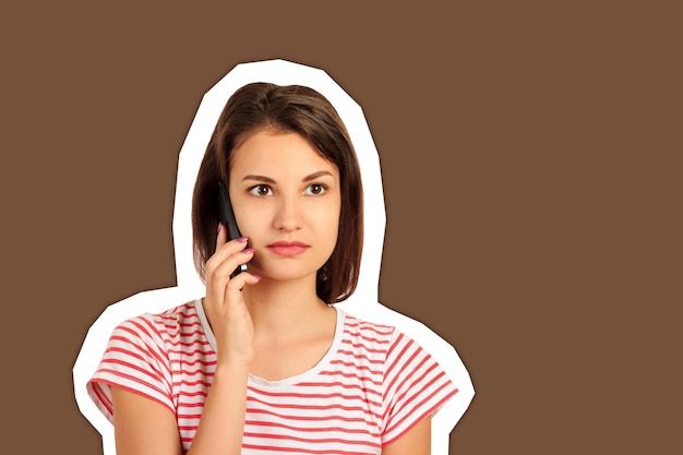 Une jeune femme attentionnée écoute le téléphone sur un fond brun.