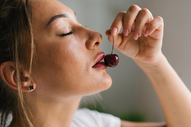 Une jeune femme attirante mange des cerises fraîches en gros plan de baies saines