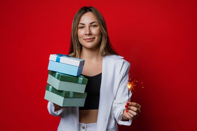 La jeune femme attirante tient des cierges magiques et des cadeaux de nouvelle année sur un fond rouge