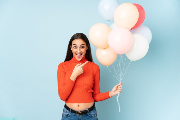 Jeune femme attraper de nombreux ballons sur le mur bleu, pointant le doigt sur le côté