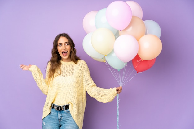 Photo jeune femme attraper de nombreux ballons sur mur violet avec une expression faciale surprise