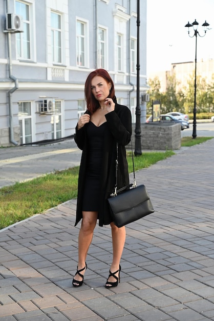 une jeune femme attrayante et confiante dans une robe noire et des chaussures à talons hauts marche dans les rues