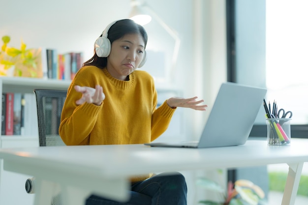 Une jeune femme attrayante utilise un ordinateur portable dans son bureau à domicile avec des écouteurs souriante et ayant l'air malheureuse et inquiète