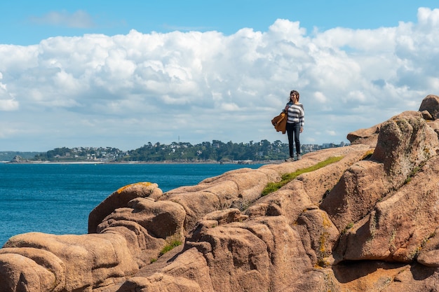 Une jeune femme au bord de la mer sur la côte à côté du phare Mean Ruz, port de Ploumanach, dans la ville de Perros-Guirec, Côtes-d'Armor, en Bretagne française, France.