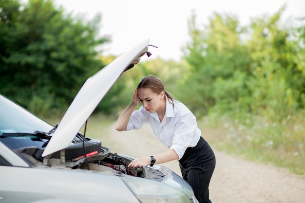 Jeune femme au bord de la route après que sa voiture soit tombée en panne Elle a ouvert le capot pour constater les dégâts