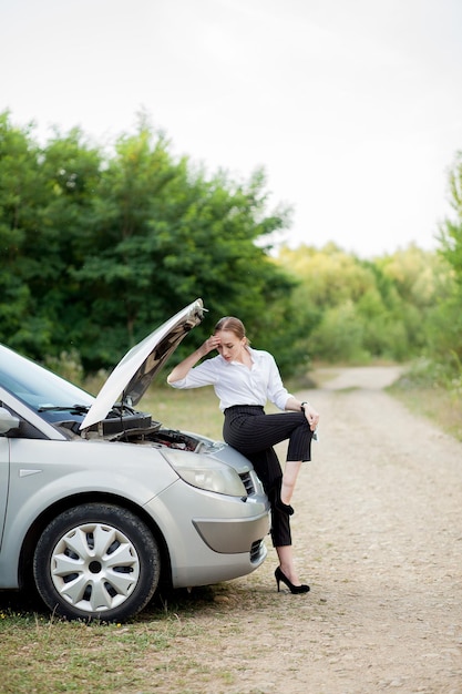 Jeune femme au bord de la route après que sa voiture soit tombée en panne Elle a ouvert le capot pour constater les dégâts