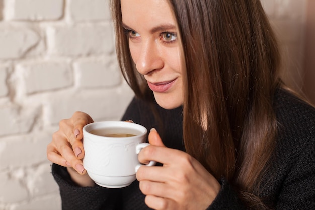 Jeune femme au café buvant ici du thé boisson préférée dans une tasse blanche