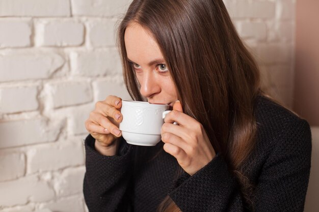 Jeune femme au café buvant ici du thé boisson préférée dans une tasse blanche