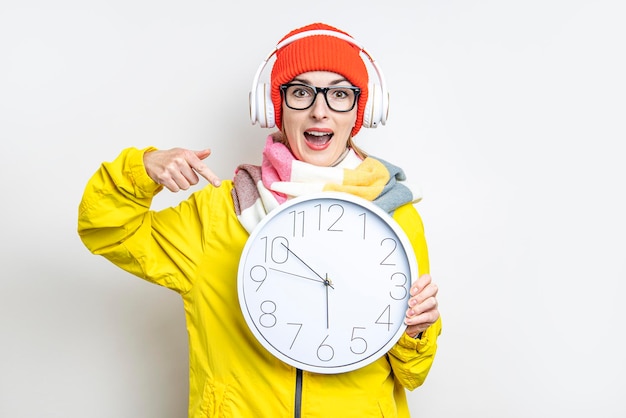 Jeune femme au casque surprise pointant son doigt vers l'horloge sur fond clair.