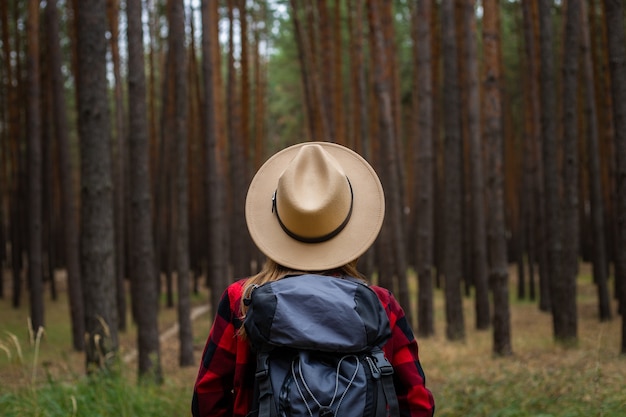 Jeune femme au chapeau, chemise rouge et sac à dos avec dans une forêt de pins. Camping dans les bois.