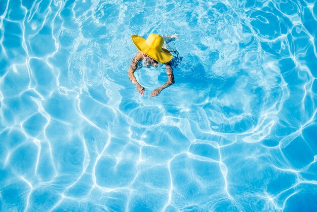 Jeune femme au chapeau jaune nageant dans le bassin aux eaux bleues. Vue générale d'en haut