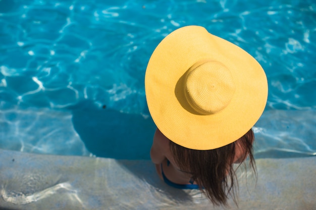 Jeune femme au chapeau jaune se détendre à la piscine