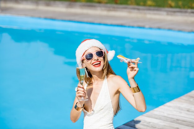 Jeune femme au chapeau de Noël et maillot de bain jouant avec un avion jouet à la piscine. Concept de vacances d'hiver