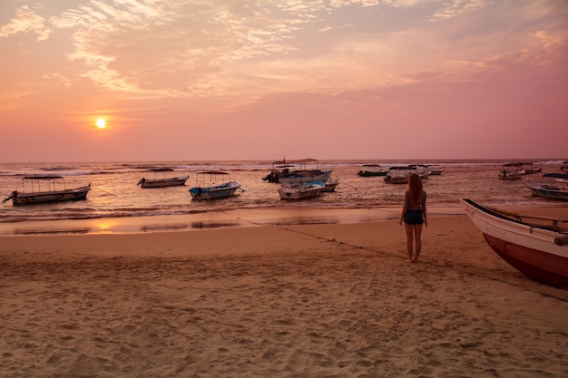 Jeune femme au chapeau regardant le coucher de soleil dans l'océan