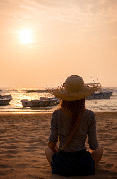 Jeune femme au chapeau regardant le coucher de soleil dans l'océan