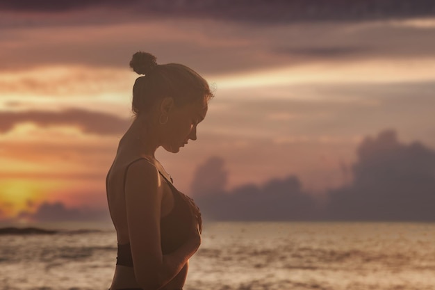 Jeune femme au coucher du soleil fait du yoga pour un mode de vie sain sur la mer tropicale ou la plage de l'océan à l'extérieur