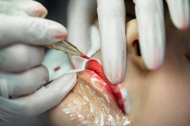 Jeune femme au cours de la procédure de maquillage permanent professionnel rougir les lèvres