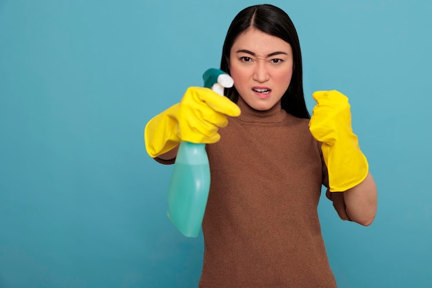 Jeune Femme Au Foyer Asiatique Frustrée En Colère Dans Des Gants En Caoutchouc Et Un Spray Détergent Debout Dans Une Pose De Combat, Concept De Maison De Nettoyage, Femme De Ménage énergique Agressive Se Sentant Négative