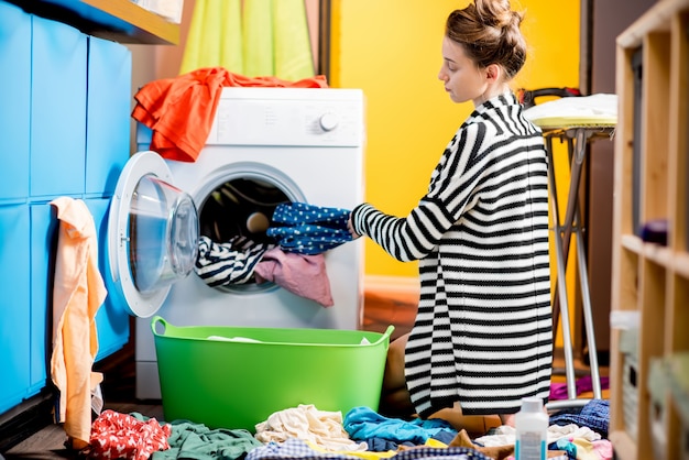 Jeune femme au foyer chargeant des vêtements dans la machine à laver assise par terre à la maison