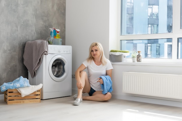 Une jeune femme au foyer avec machine à laver et vêtements. Jour de lessive.