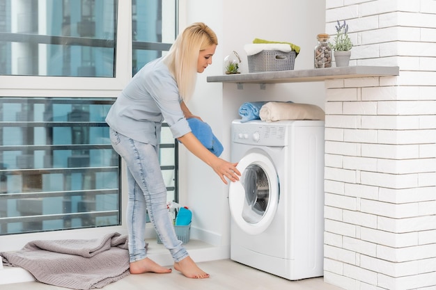 Une jeune femme au foyer avec machine à laver et vêtements. Jour de lessive.