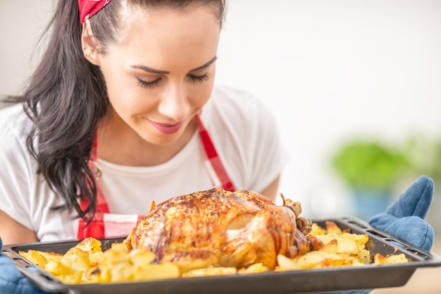 La jeune femme au foyer sent le poulet fraîchement cuit et les pommes de terre d'un plateau.