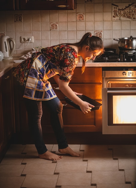 Jeune femme au foyer tenant des cookies sur une casserole près du four