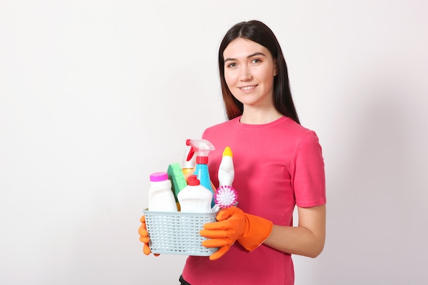 Une jeune femme au foyer tient dans ses mains des produits de nettoyage sur un fond coloré