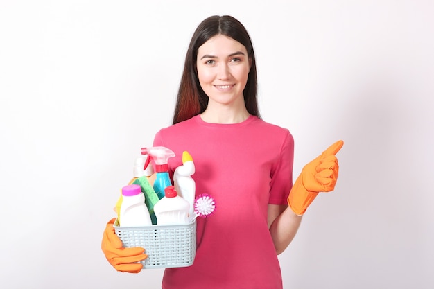 Une jeune femme au foyer tient dans ses mains des produits de nettoyage sur un fond coloré