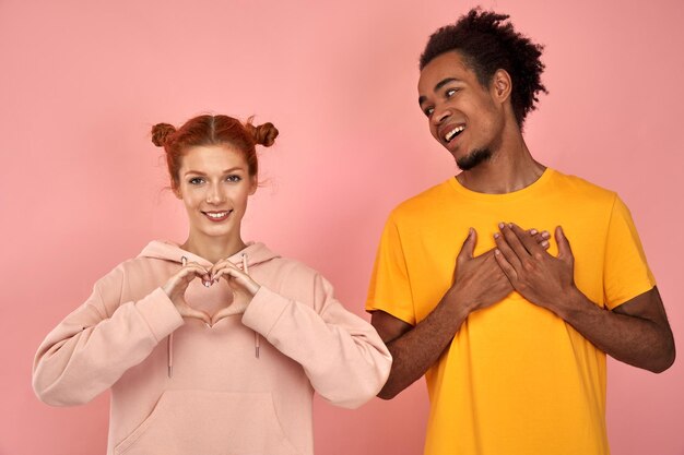 Photo une jeune femme au gingembre romantique et affectueuse et un homme à la peau foncée font des gestes cardiaques